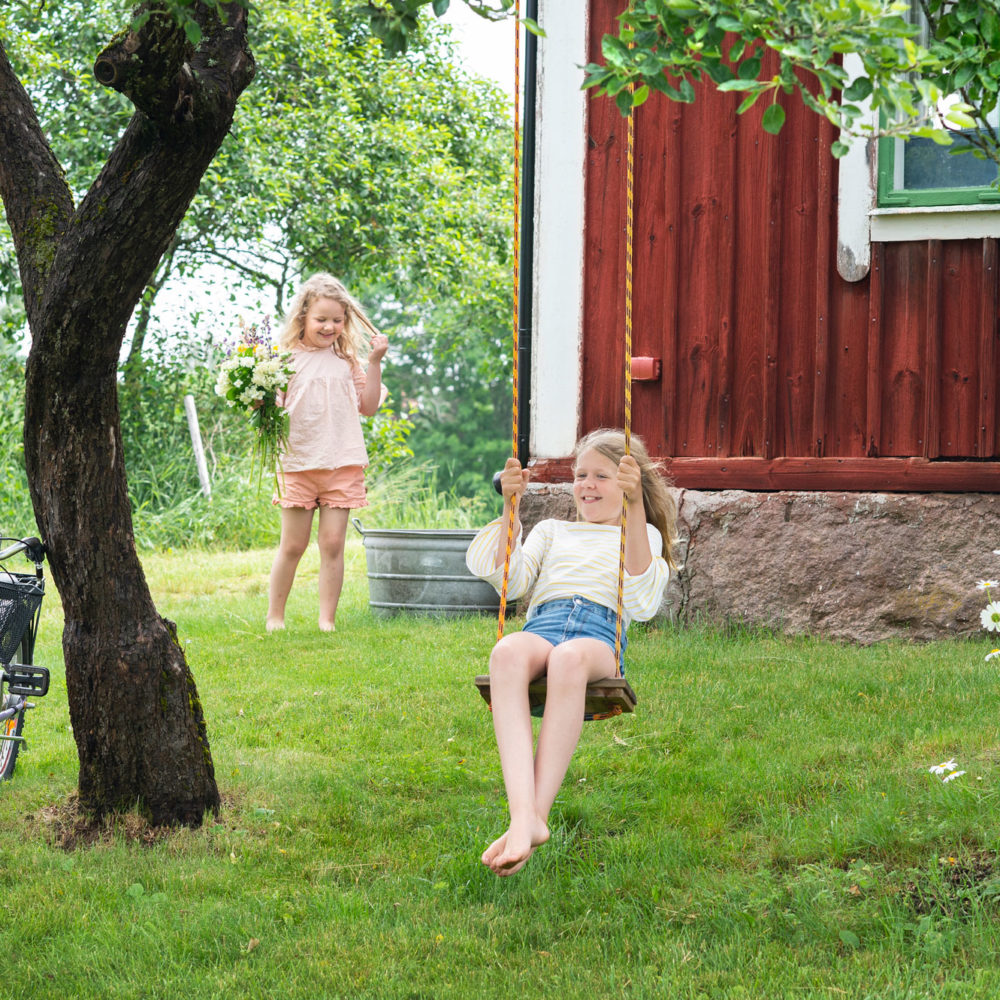 Zwei Kinder spielen im Garten auf einer Schaukel