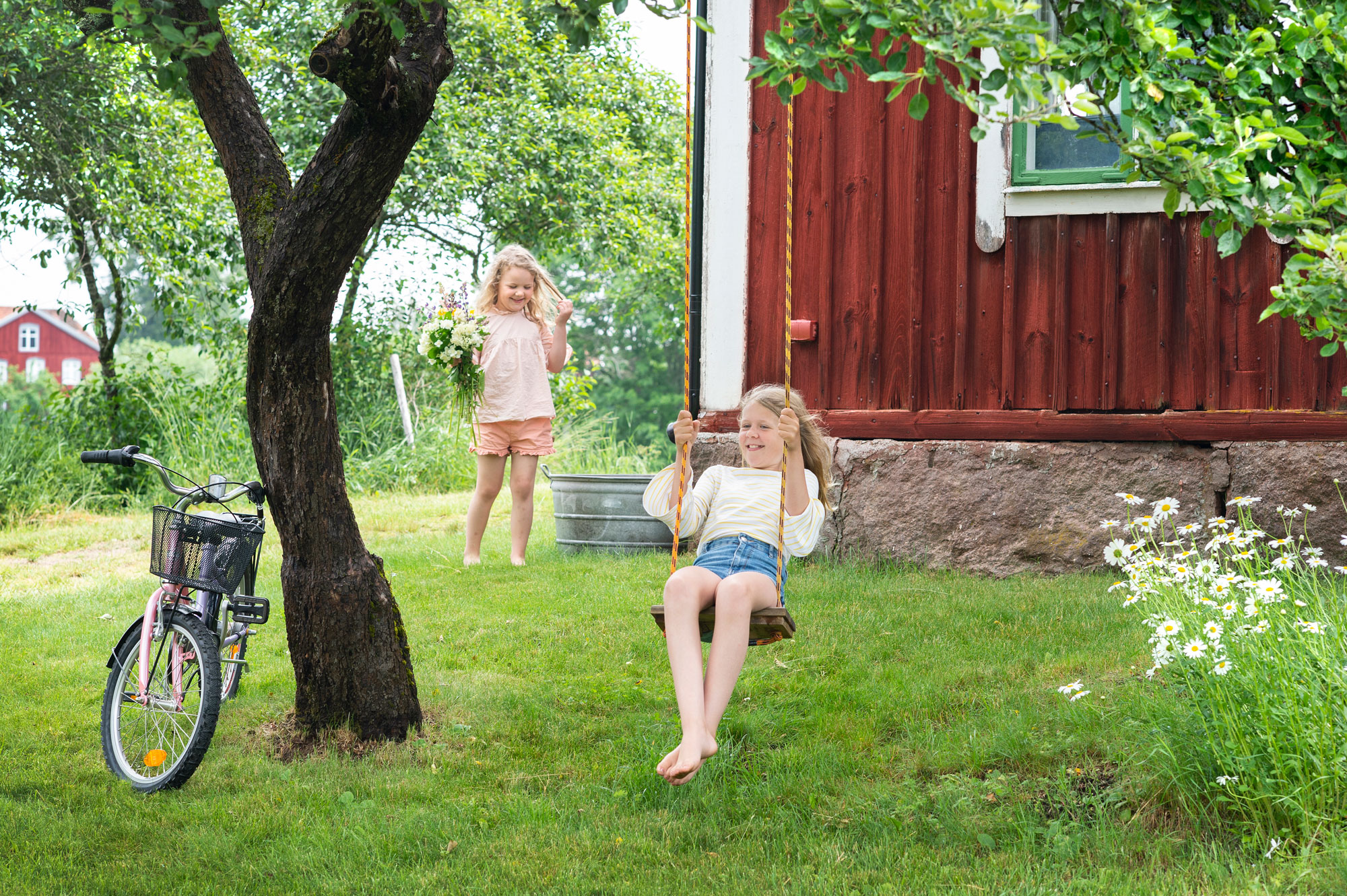 Zwei Kinder spielen im Garten auf einer Schaukel