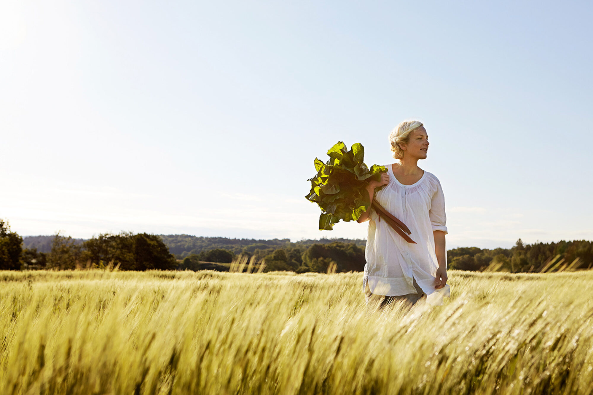 Bild på en kvinna med blommor i handen ute på en äng.