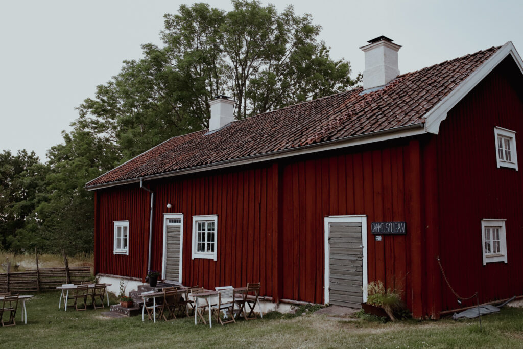 Ett rött hus med vita fönster och dörrar. Utanför står stolar och bord.