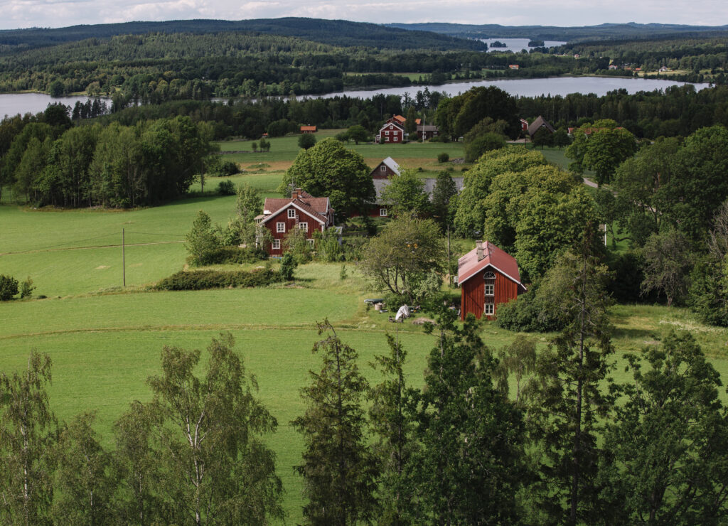 Vogelperspektive auf die schwedische Landschaft mit Wiesen, Wäldern, Seen und roten Holzhäusern.