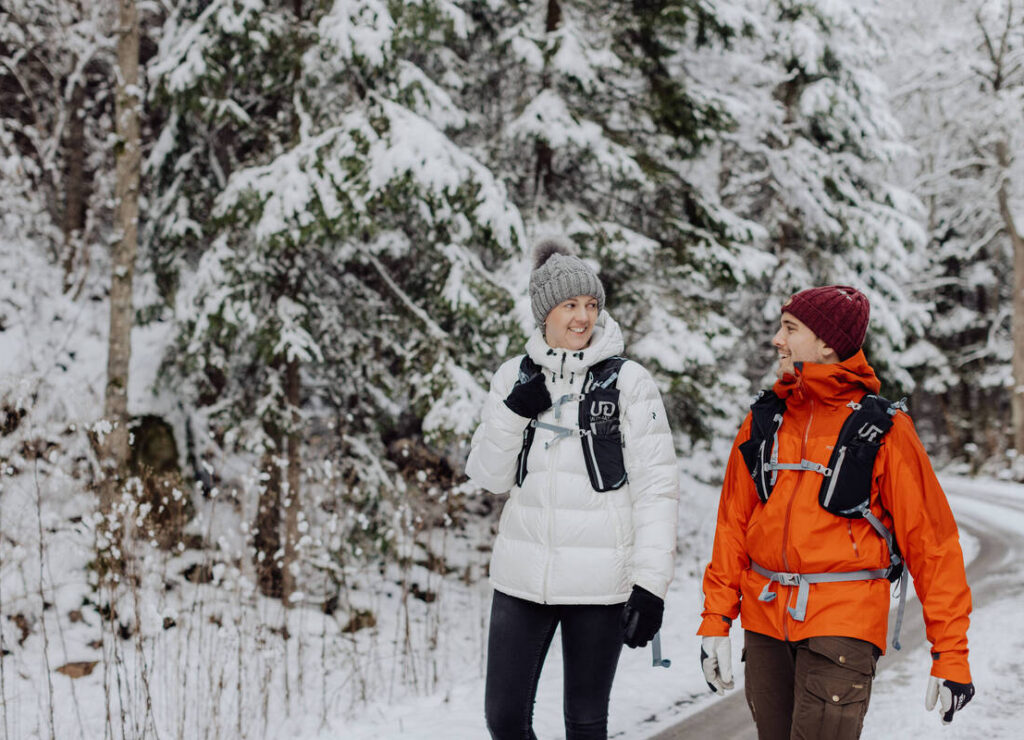 Eine Frau und ein Mann wandern durch eine verschneite Waldlandschaft.